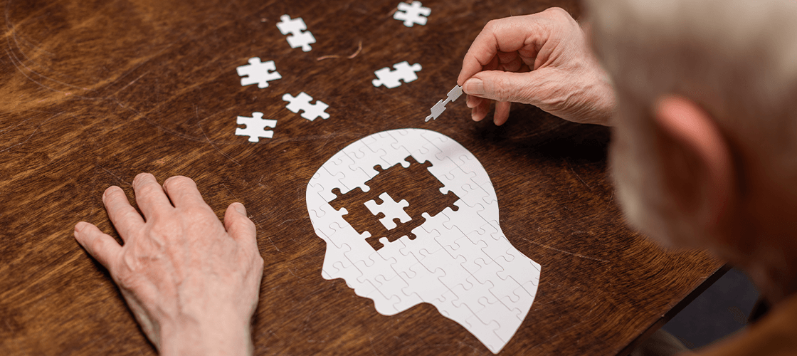 Man sitting at table, sharpening his mind by adding puzzle pieces to a puzzle in the shape of a human head